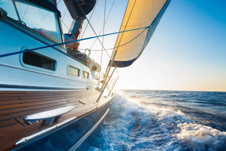 Sailing yacht underway at sea with mainsail filled by wind, viewed from the teak side deck as waves break along the hull. The image illustrates real offshore sailing conditions and the loads experienced by rigging systems, including standing rigging, mast fittings, and hydraulic or mechanical components supplied by Navtec. Such conditions highlight the importance of proper inspection, maintenance, and replacement of sailing yacht rigging hardware to ensure safety and performance.