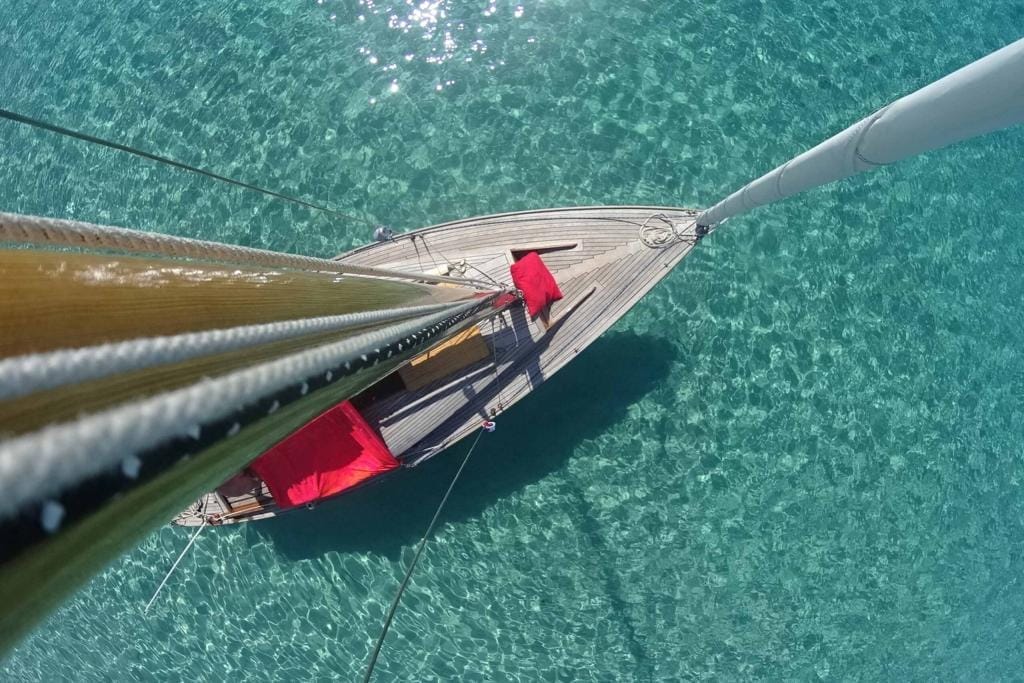 A yacht on an azure sea viewed from the top of the mast above