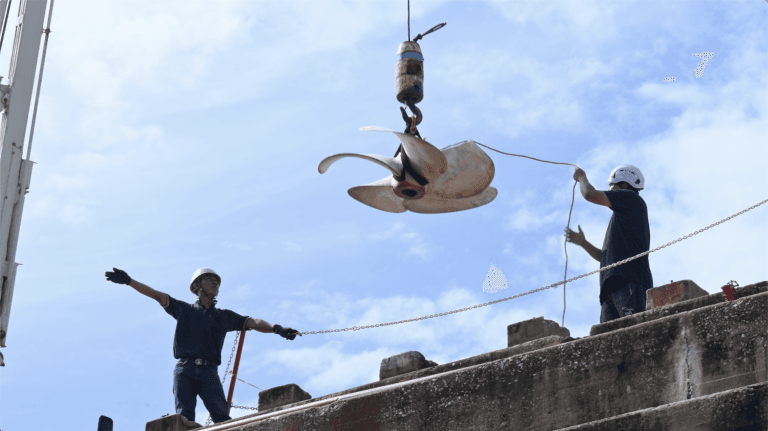 superyacht propeller being craned overhead 2 engineers in a bangkok dry superyacht refit dry dock