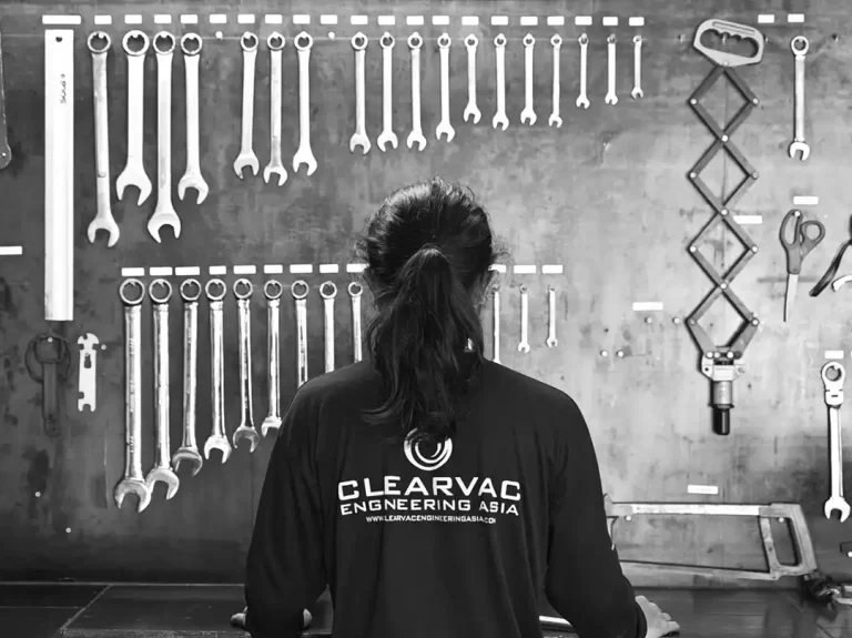 A marine Mechanical engineer is seen from behind at a workshop table with spanners and other marine tools displayed on the wall