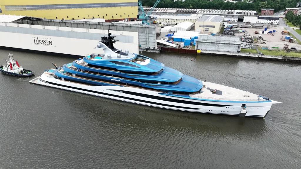 Lürssen superyacht Deep Blue during launch at Bremen shipyard in June 2025, showcasing its distinctive blue superstructure, white hull, and tiered aft decks with helipad and pool.