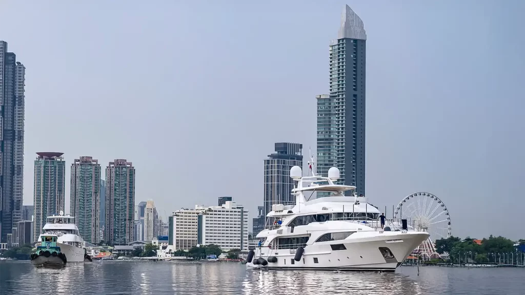 Luxury superyacht cruising on the Chao Phraya River in Bangkok with city skyscrapers and the Ferris wheel in the background. Image represents Clearvac Engineering Asia’s superyacht refit, maintenance, and marine engineering services in Thailand.